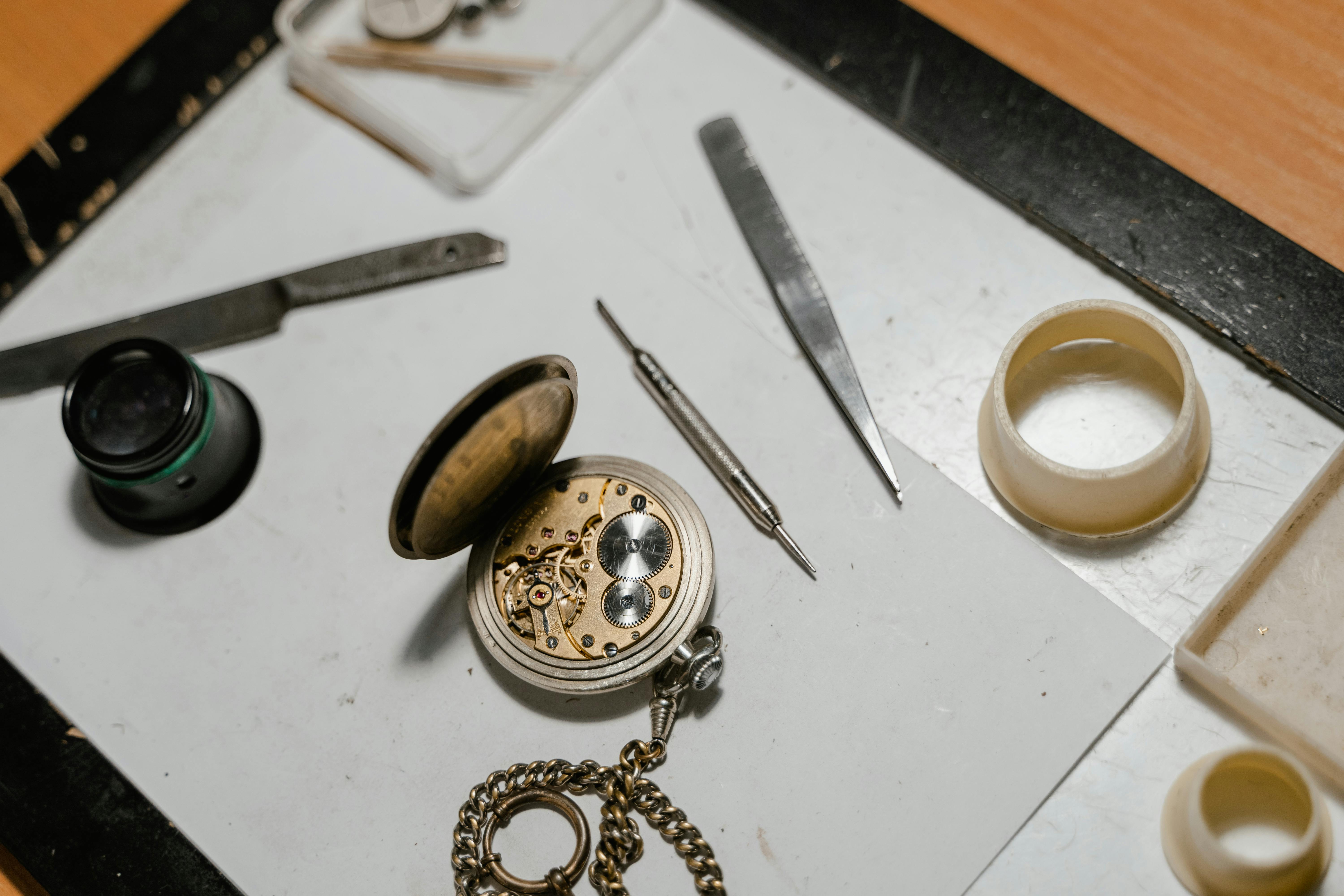 Open pocket watch with loupe, tweezers, and movement holder on a watchmaker's bench